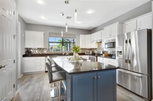 a kitchen with stainless steel appliances granite countertop a refrigerator a sink dishwasher a stove and white cabinets with wooden floor