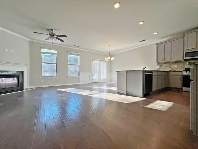 an empty room with wooden floor kitchen view and a window