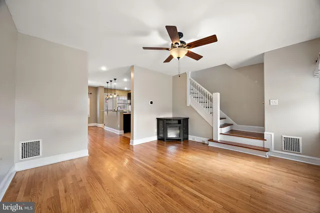 a view of an empty room with wooden floor and a ceiling fan