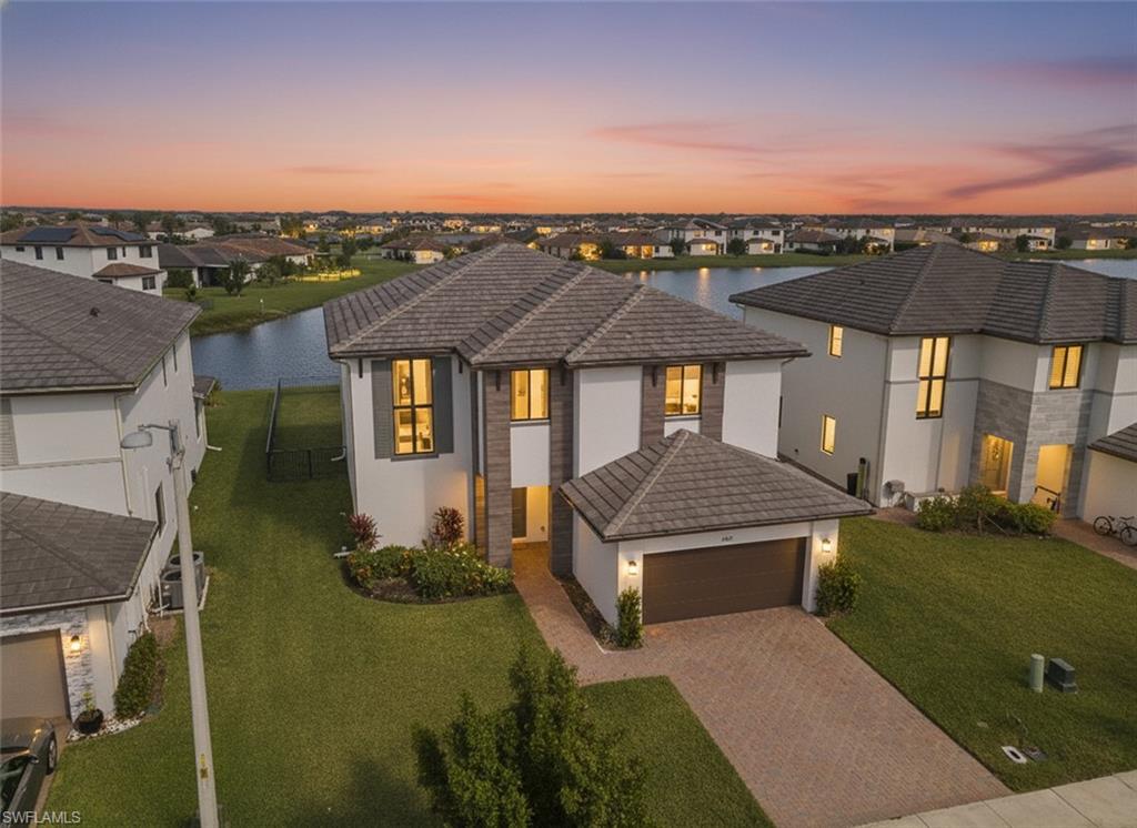 View of front of home featuring a tile roof, stucco siding, a yard, and decorative driveway