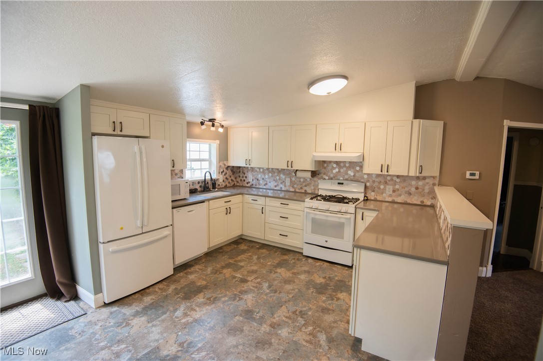 4594 Center Road Andover, OH 44003 - Photo 4 of 39 Kitchen featuring white appliances, a peninsula, lofted ceiling, decorative backsplash, and a textured ceiling
