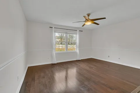 an empty room with wooden floor ceiling fan and windows