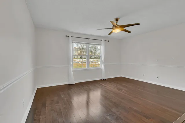 an empty room with wooden floor ceiling fan and windows
