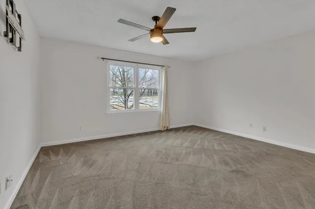 an empty room with chandelier fan and windows