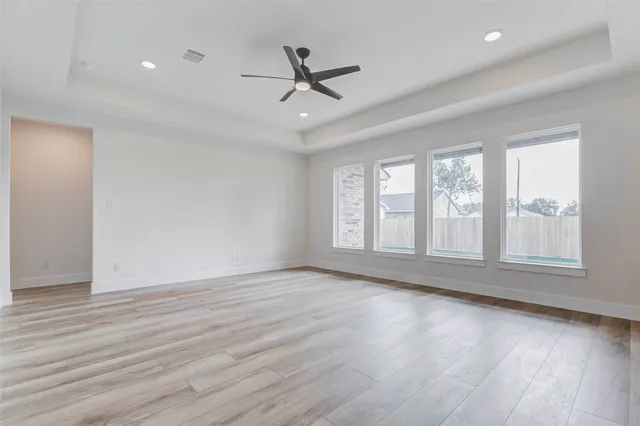 an empty room with wooden floor fan and windows