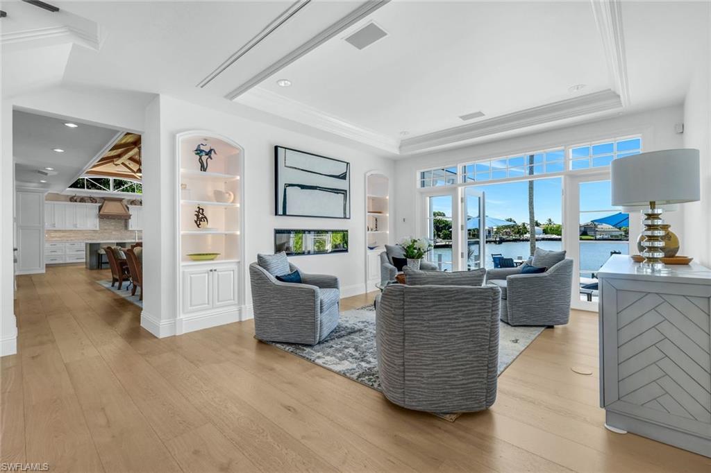 400 Springline Drive Naples, FL 34102 - Photo 12 of 37 Living room featuring light wood-style flooring, a water view, built in features, a fireplace, and ornamental molding
