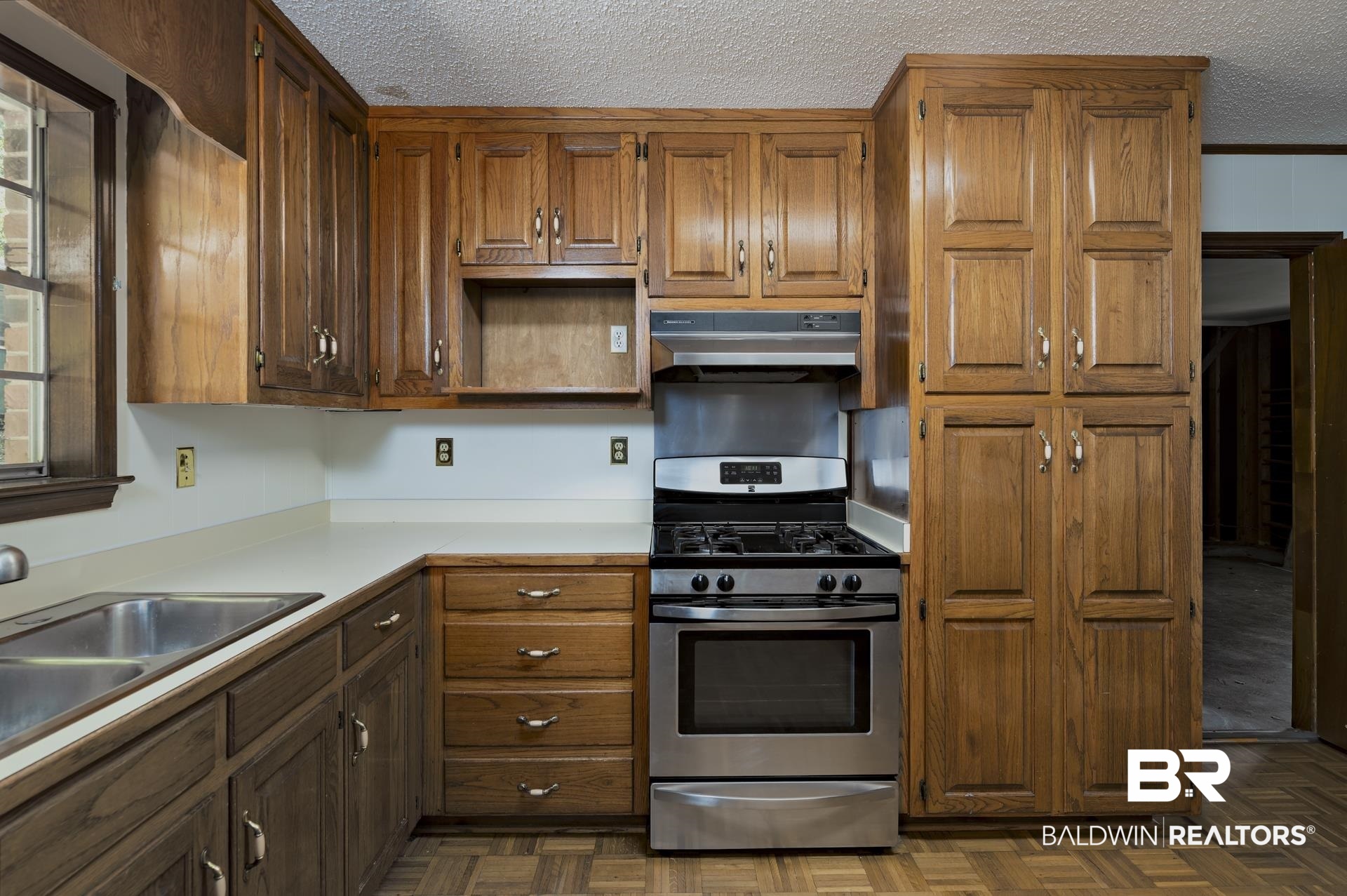 707 Johnson Avenue Fairhope, AL 36532 - Photo 20 of 38 Kitchen with light countertops, stainless steel gas range oven, a textured ceiling, under cabinet range hood, and brown cabinets