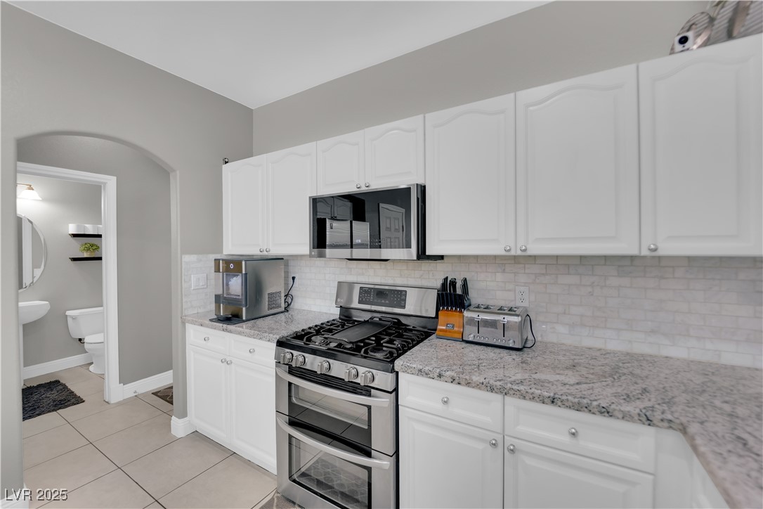 9005 Rendon Street Las Vegas, NV 89143 - Photo 12 of 51 Kitchen with appliances with stainless steel finishes, backsplash, white cabinets, and light stone countertops