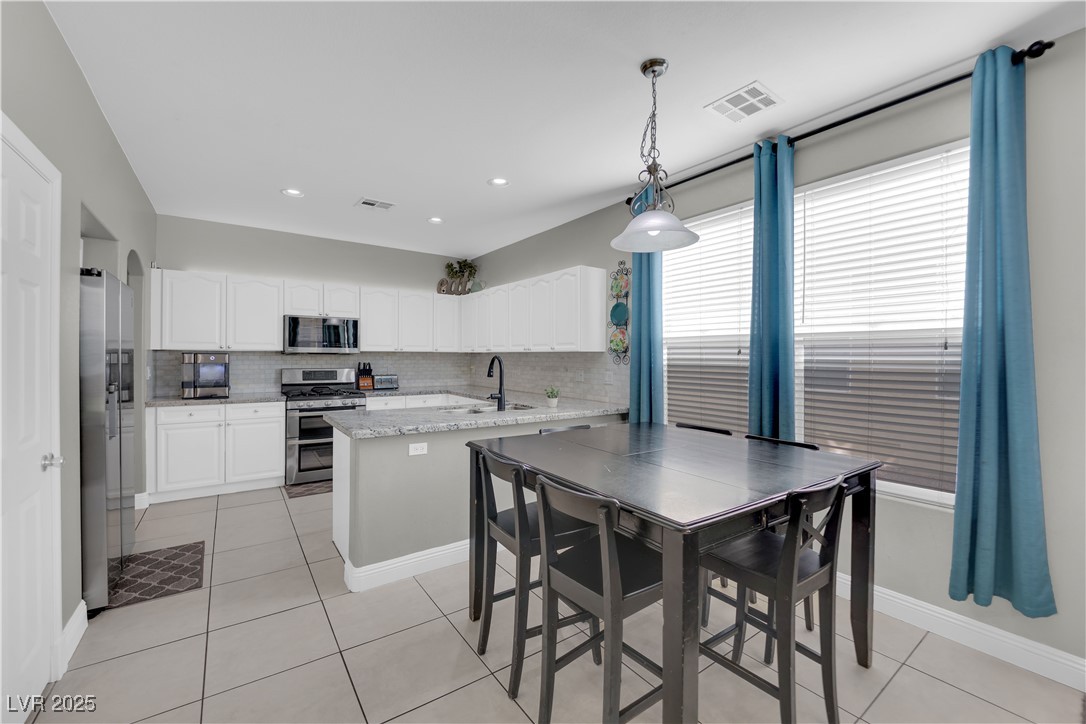 9005 Rendon Street Las Vegas, NV 89143 - Photo 8 of 51 Kitchen with white cabinetry, light tile patterned floors, appliances with stainless steel finishes, a peninsula, and decorative backsplash
