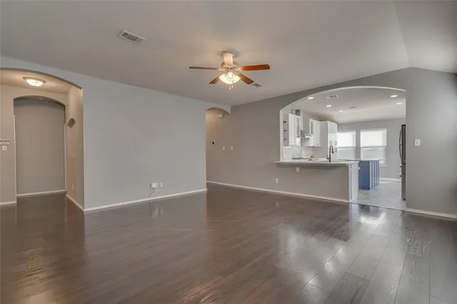 a view of an empty room with wooden floor and a ceiling fan