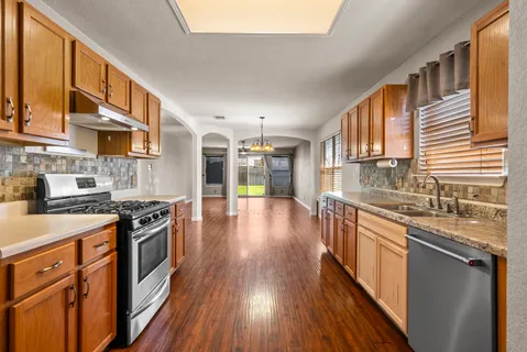 a kitchen with stainless steel appliances granite countertop hardwood floor sink stove and wooden cabinets