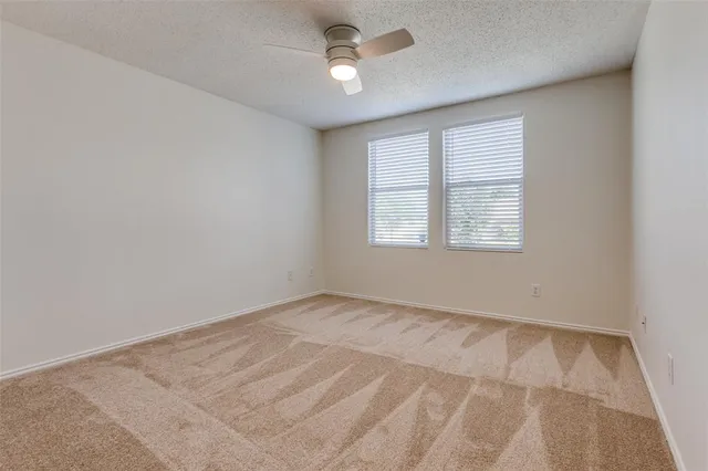 an empty room with chandelier fan and windows