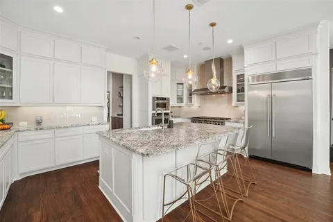 a kitchen with stainless steel appliances granite countertop a refrigerator a sink dishwasher a stove and white cabinets with wooden floor