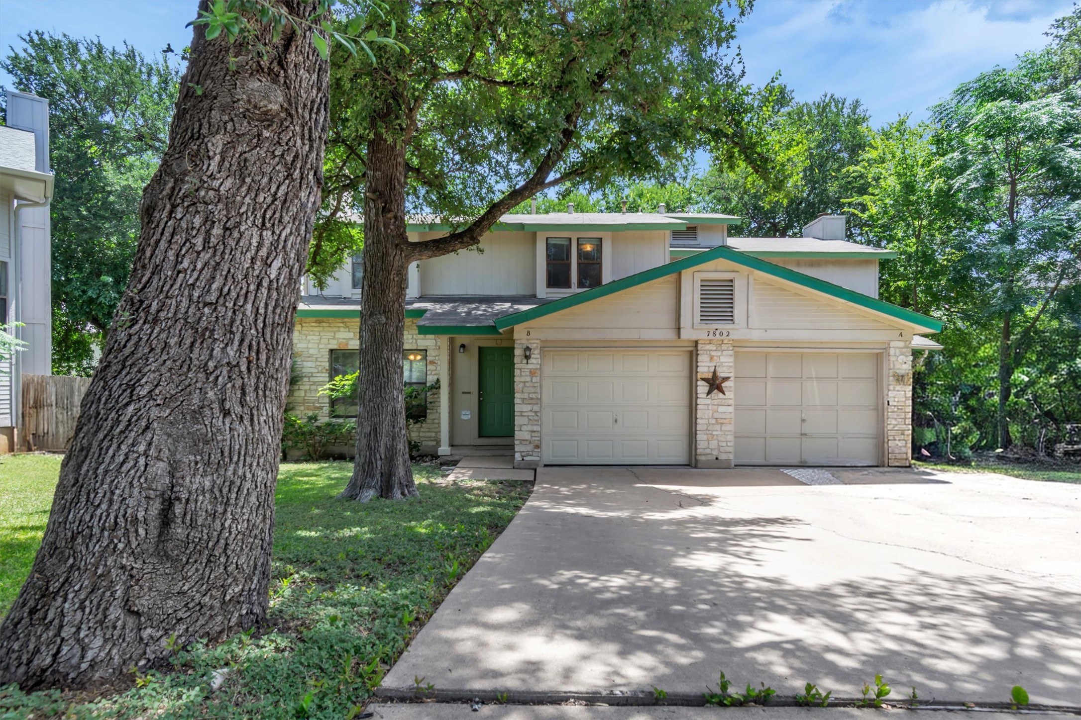 7802 Topawa Cove, Unit B Austin, TX 78729 - Photo 2 of 32 A welcoming facade features a prominent one-car garage and a charming green entry door, set amongst mature shade trees.