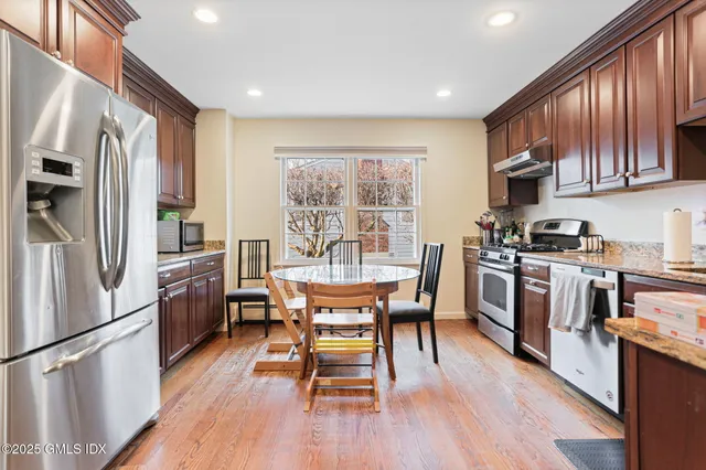 a kitchen with stainless steel appliances granite countertop a stove a refrigerator a sink dishwasher a dining table and chairs with wooden floor