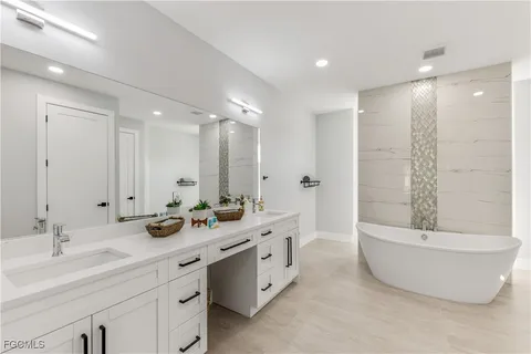 a bathroom with a double vanity sink a large mirror and a bathtub