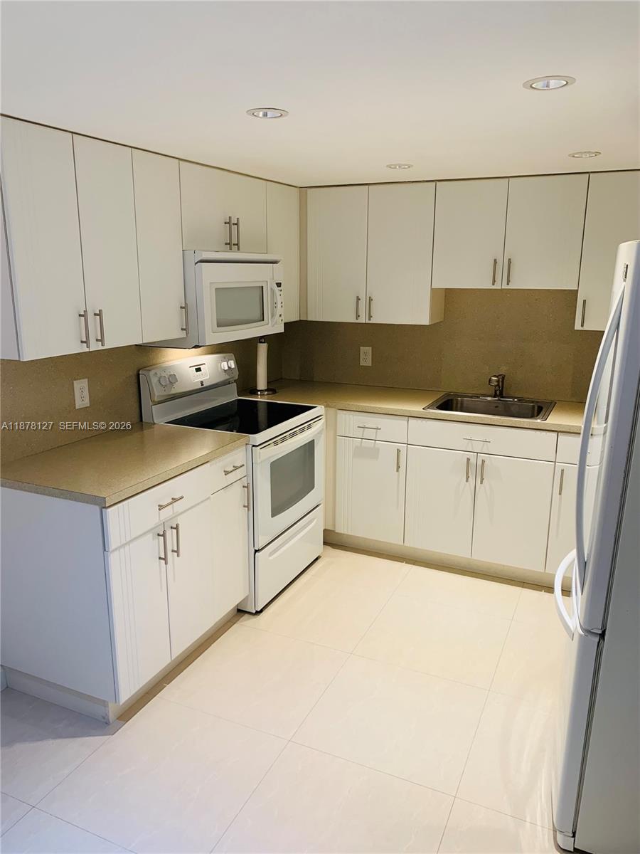 16500 Golf Club Road, Unit 101 Weston, FL 33326 - Photo 14 of 44 a kitchen with granite countertop a sink a stove and white cabinets