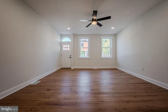 a view of empty room with wooden floor and fan