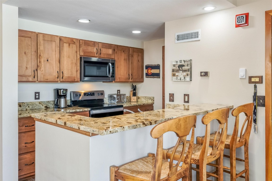 21630 Highway 6, Unit 2149 Keystone, CO 80435 - Photo 9 of 35 a kitchen with stainless steel appliances granite countertop a stove a sink a microwave a refrigerator and white cabinets with wooden floors