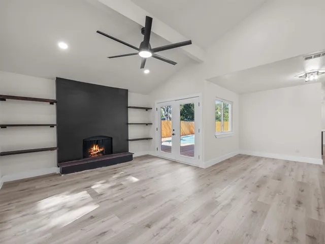 an empty room with windows a fireplace a ceiling fan and wooden floor