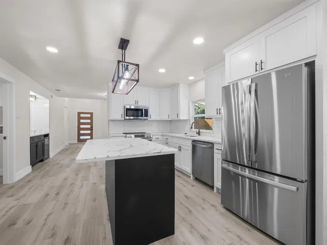 a large kitchen with stainless steel appliances granite countertop a refrigerator a stove oven a sink dishwasher and white cabinets with wooden floor