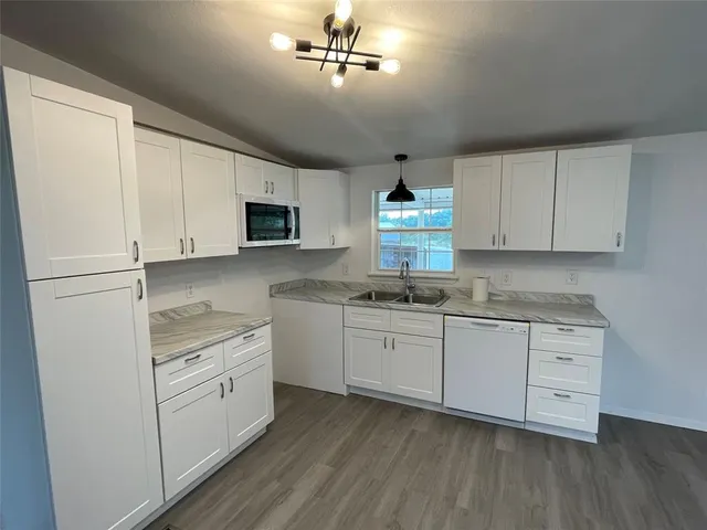 a kitchen with granite countertop white cabinets white appliances a sink and a window