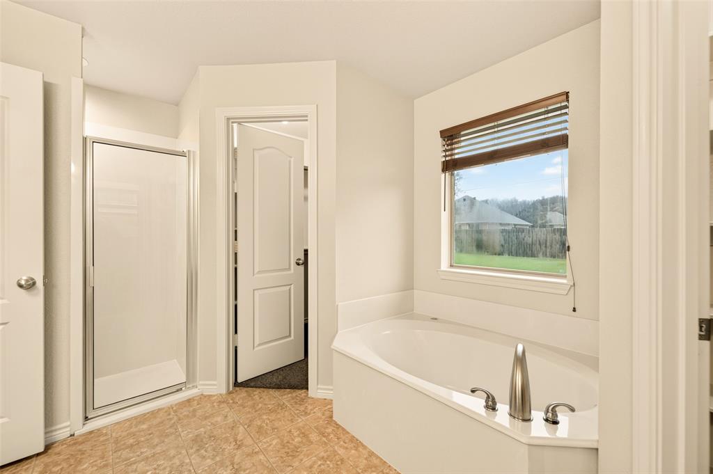 2105 Ridgewood Drive Bridgeport, TX 76426 - Photo 18 of 27 Corner soaking tub with brushed nickel fixtures, a private window with wood-finish blinds, and a tiled floor, and walk-in closet #1.