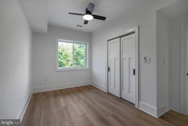 an empty room with wooden floor ceiling fan and windows