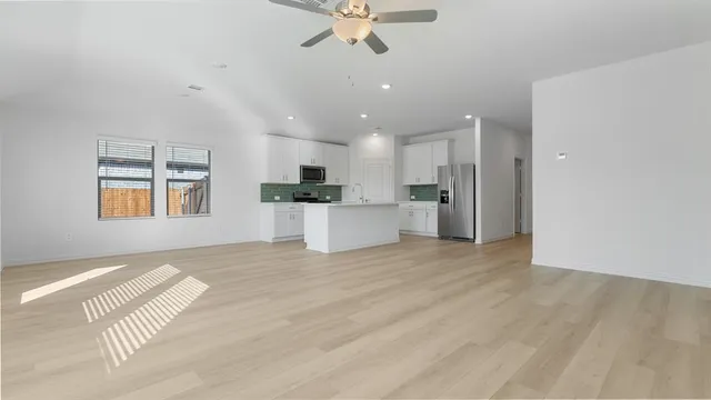 a view of an empty room with kitchen and window