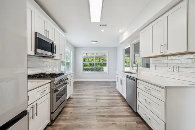 a large white kitchen with sink and stainless steel appliances
