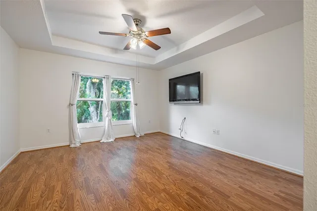 an empty room with wooden floor fan and windows