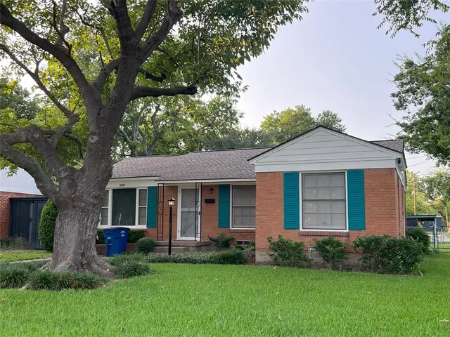a view of a brick house with a yard potted plants and a large tree