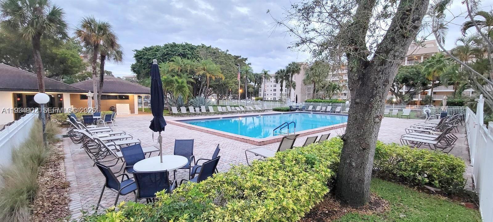 2671 South Course Drive, Unit 109 Pompano Beach, FL 33069 - Photo 38 of 39 a view of a patio with couches table and chairs under an umbrella with large trees