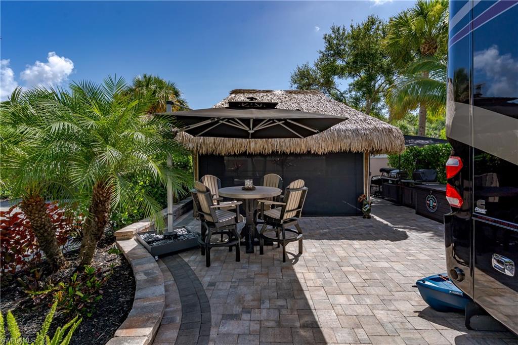 13571 Snook Circle Naples, FL 34114 - Photo 25 of 47 a view of a patio with table and chairs under an umbrella with a fire pit and potted plants