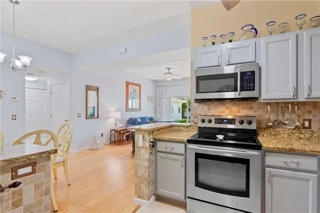 a kitchen with stainless steel appliances granite countertop a stove a microwave a sink a refrigerator and white cabinets with wooden floor