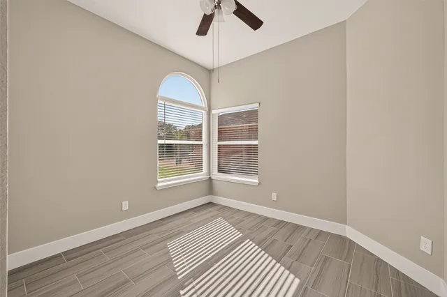 an empty room with wooden floor chandelier fan and windows