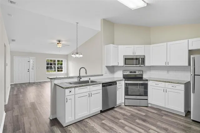 a kitchen with stainless steel appliances granite countertop a sink stove oven and white cabinets with wooden floor