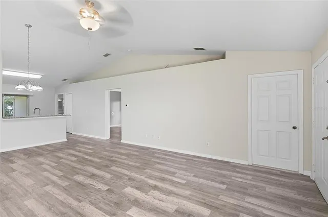 a view of an empty room with a chandelier fan and kitchen view