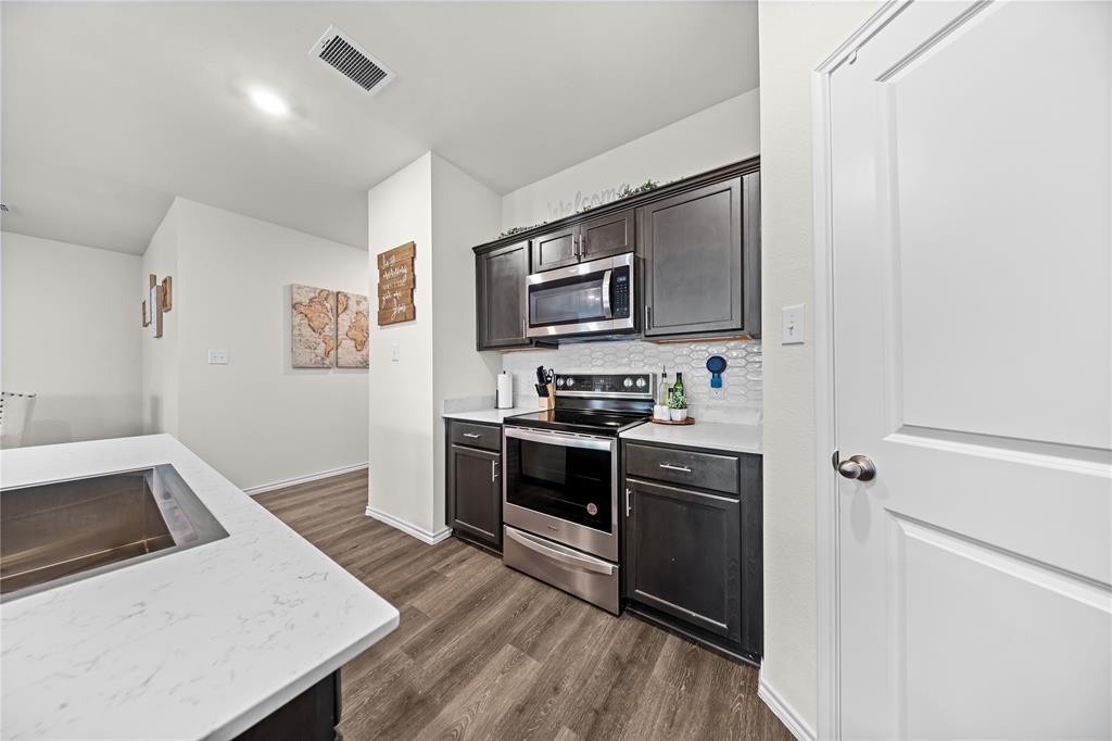 2920 Roper Street Royse City, TX 75189 - Photo 12 of 29 Kitchen featuring dark wood-finish cabinetry, stainless steel appliances including a microwave and range, light-toned countertops, and a white hexagonal tile backsplash