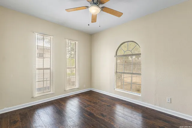 an empty room with wooden floor chandelier fan and windows