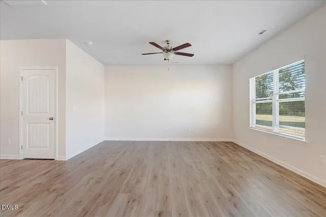 an empty room with wooden floor ceiling fan and windows