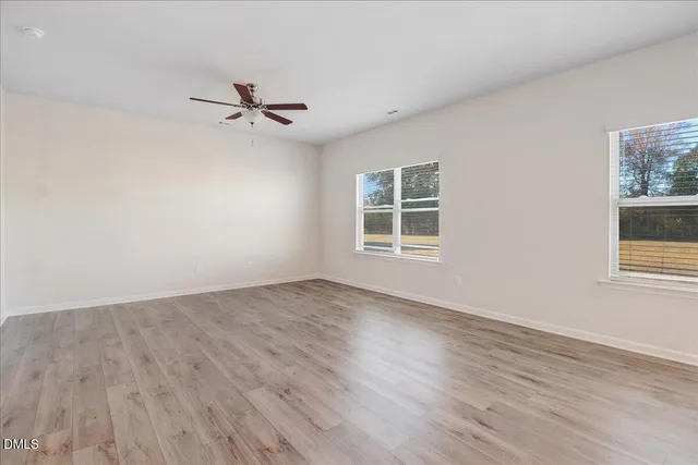 an empty room with wooden floor ceiling fan and windows
