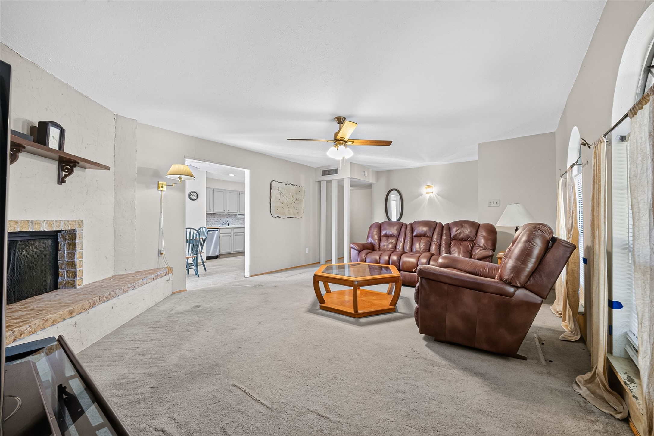 22926 Millgate Drive Spring, TX 77373 - Photo 9 of 34 This cozy living room features a plush sectional sofa, a ceiling fan, and a fireplace with a built-in shelf. Natural light streams in through large windows, and the open layout leads to a bright kitchen.