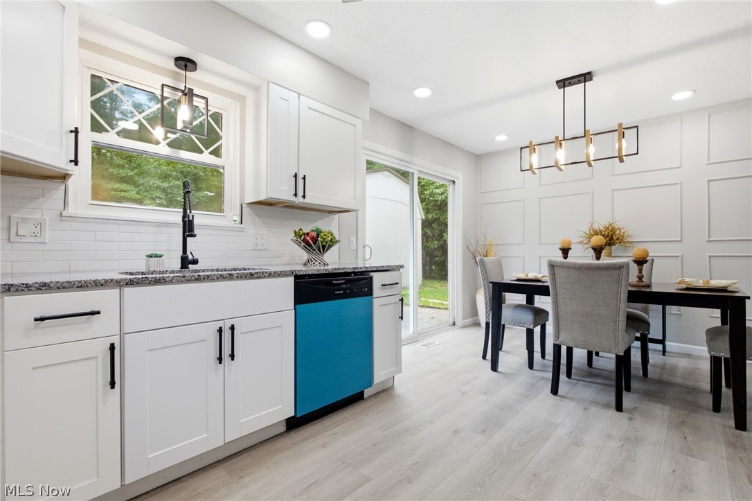 White shaker cabinetry, granite countertops, subway tile backsplash, wood-finish flooring, and a sliding glass door