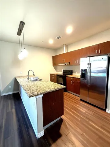 a view of a kitchen with kitchen island a sink wooden floor and black appliances