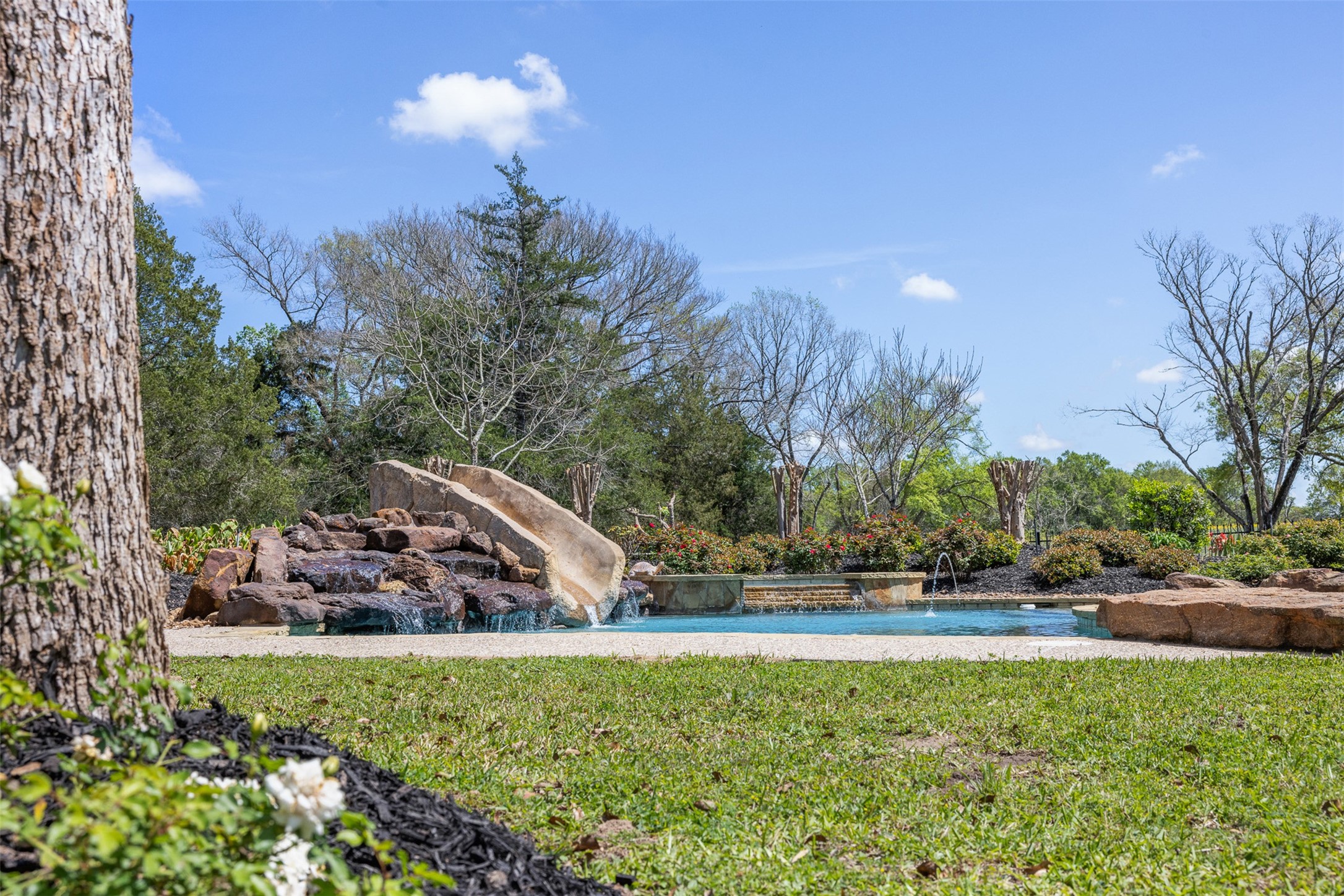 29500 Skymac Ranch Road Hempstead, TX 77445 - Photo 40 of 50 Framed by established trees and open green space, the pool showcases a striking rock waterfall and slide, offering a setting that feels both private and thoughtfully designed.