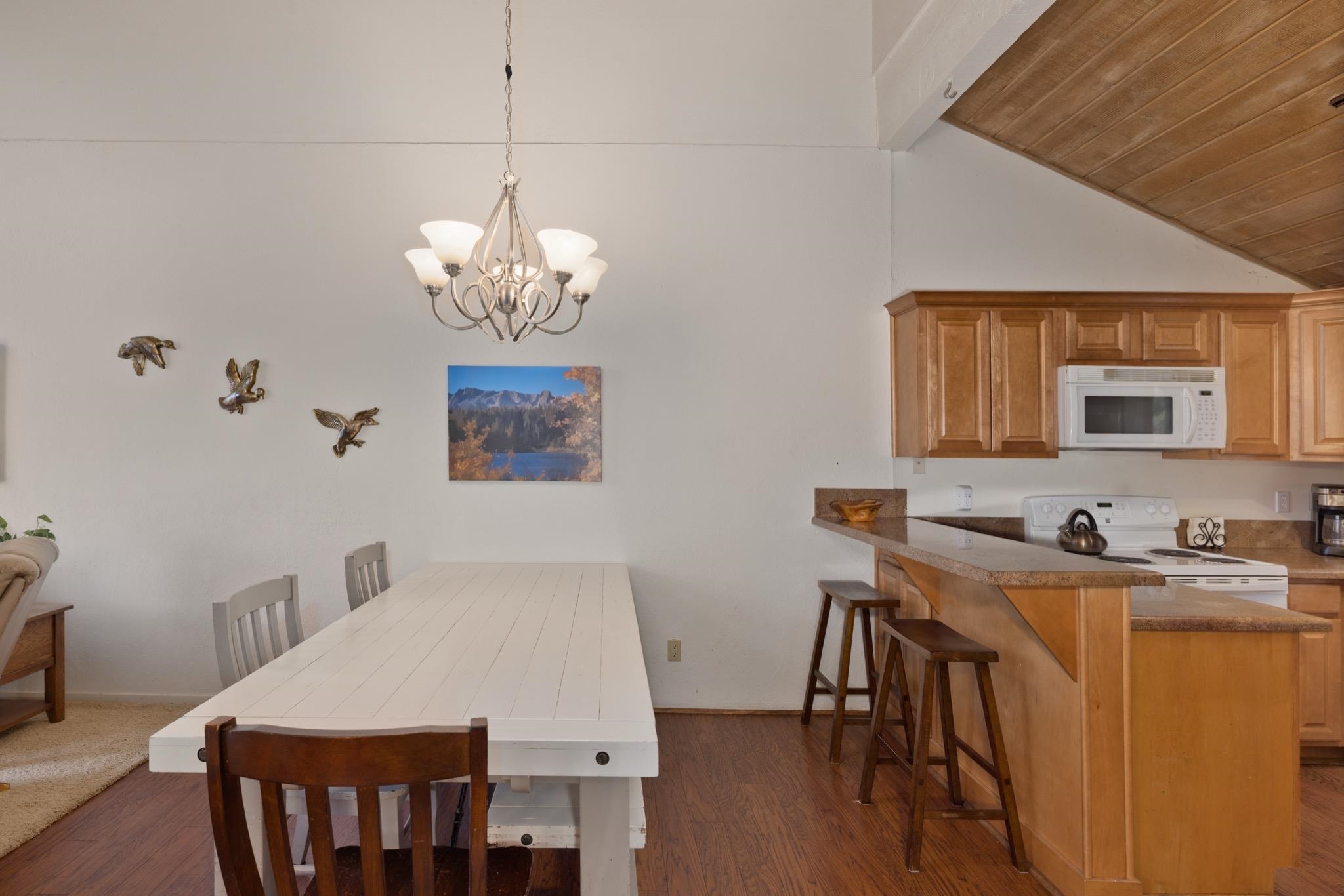 3392 Chateau Road, Unit 29 Mammoth Lakes, CA 93546 - Photo 12 of 30 Open-concept living area with wood-finish flooring, a contemporary chandelier, and a kitchen featuring wood cabinetry, a breakfast bar, and white appliances