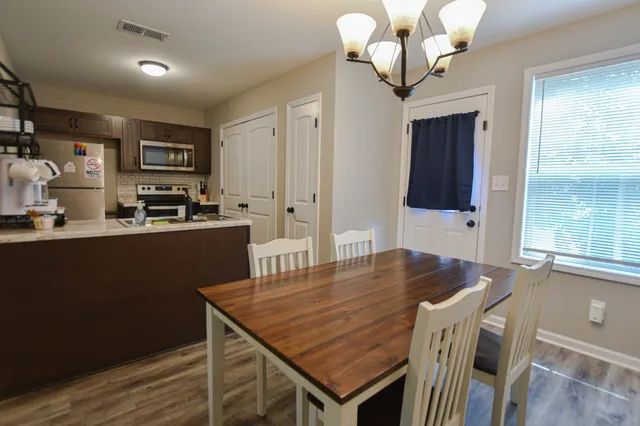 a kitchen with stainless steel appliances granite countertop a stove a refrigerator a sink a dining table and chairs with wooden floor