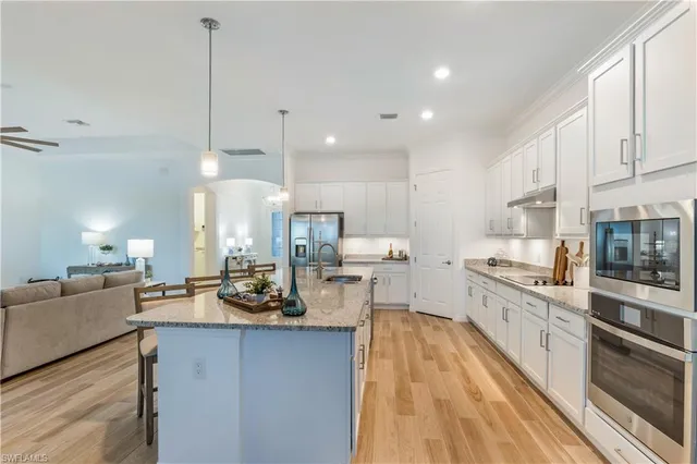 a large kitchen with stainless steel appliances a large counter top a stove a sink dishwasher a dining table and chairs with wooden floor