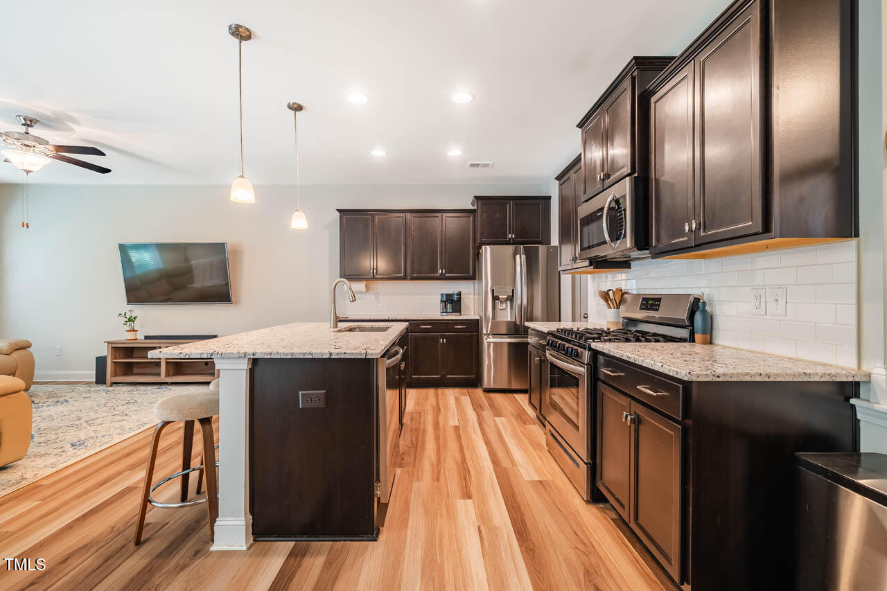 1101 Compass Drive Durham, NC 27713 - Photo 7 of 32 a kitchen with stainless steel appliances granite countertop a stove top oven a sink dishwasher a dining table and chairs with wooden floor